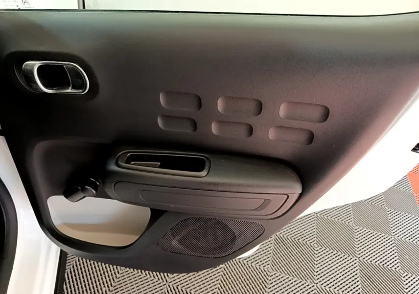 Vue rapprochée de la porte intérieure côté conducteur noire avec poignée et haut-parleur de la Citroën C3 blanche.