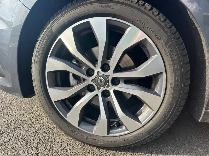 Gros plan sur la jante alu gris argentée avec logo Renault au centre, montée sur un pneu Michelin d’un Renault Mégane Break gris Titanium.