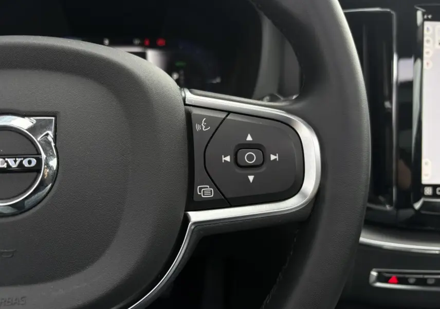 Gros plan sur le côté droit du volant noir du Volvo XC60 2024 avec commandes intégrées et écran tactile en arrière-plan.