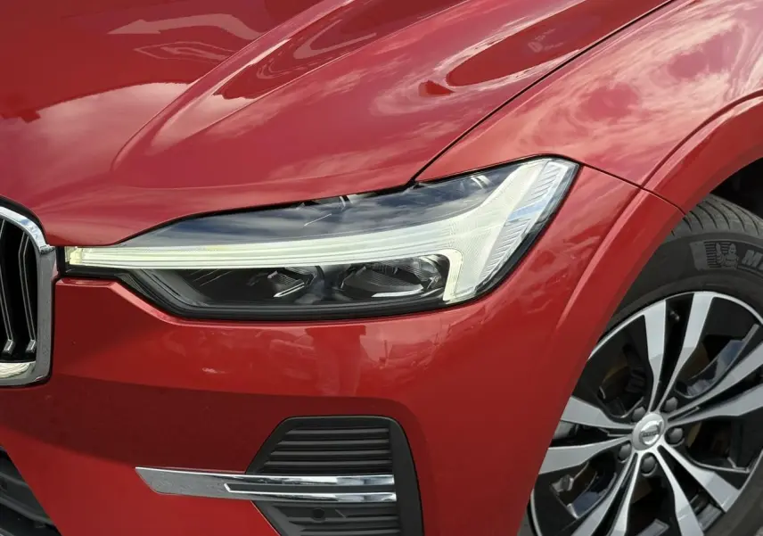 Gros plan sur l'avant droit du Volvo XC60 rouge Fusion 2024, mettant en valeur le phare LED et la jante alliage.