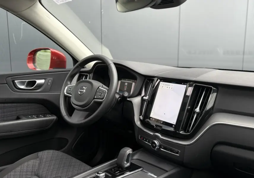 Vue intérieure côté conducteur du Volvo XC60 T6 AWD PHEV 2024, volant noir, écran tactile vertical et rétroviseur rouge visible.