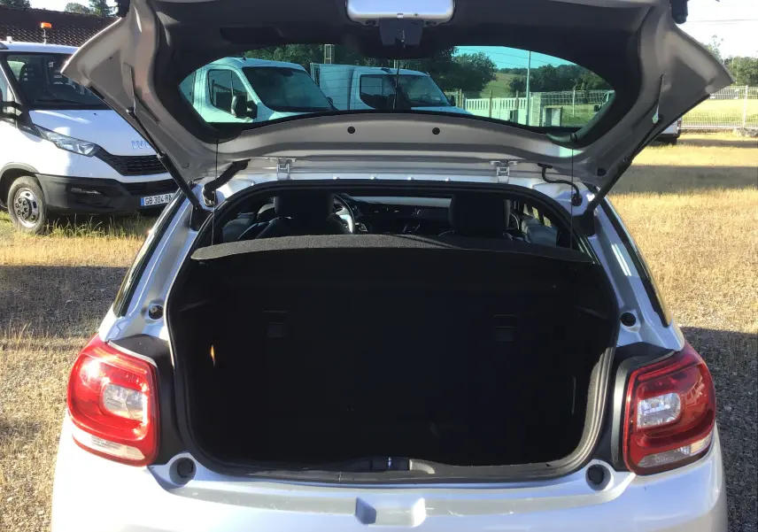Vue arrière d'une Citroën DS3 gris clair métal de 2013 avec coffre ouvert, montrant l'espace de chargement et les feux arrière.