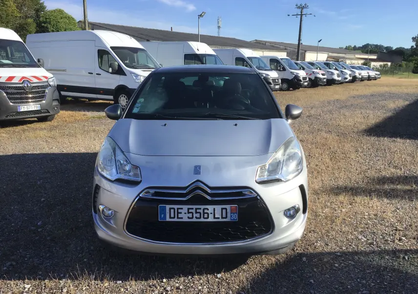 Citroën DS3 gris clair métal vu de face, avec calandre distinctive et phares arrondis, stationné sur un terrain.