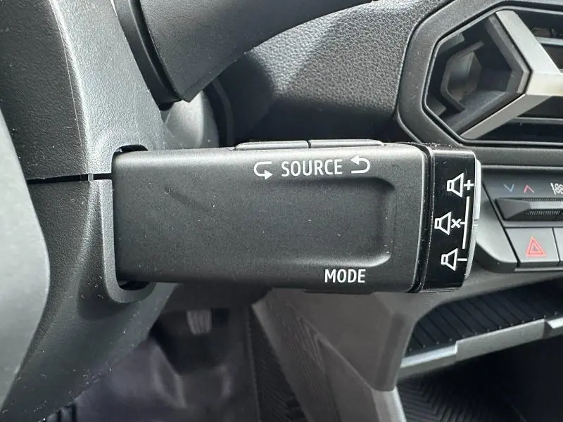 Gros plan sur la commande au volant droite du Dacia Duster 2025, avec boutons source et mode visibles dans l’habitacle noir.