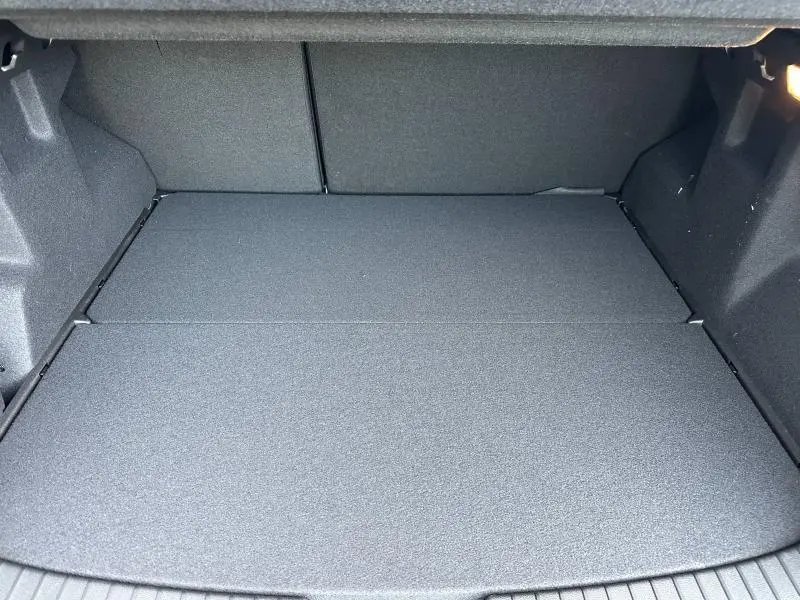 Coffre spacieux et vide du Dacia Duster 1.8 hybrid 155ch Journey 2025, vu de face, avec revêtement gris foncé uniforme.