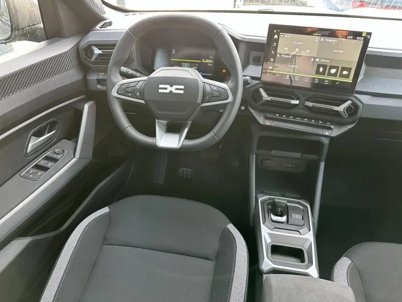 Vue intérieure frontale du poste de conduite du Dacia Duster 2025, avec volant multifonction et écran tactile central.