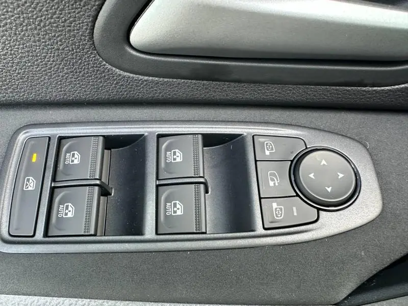 Gros plan sur les commandes des vitres électriques et rétroviseurs du côté gauche d'un Dacia Duster 1.8 hybrid noir nacré 2025.