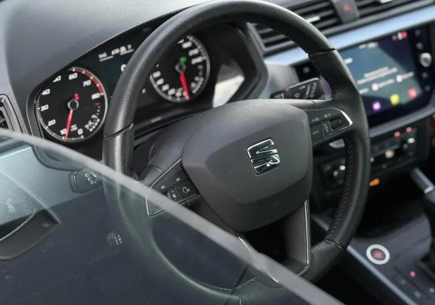 Vue rapprochée du volant en cuir noir d'une SEAT Arona 2020, avec tableau de bord et écran tactile en arrière-plan.