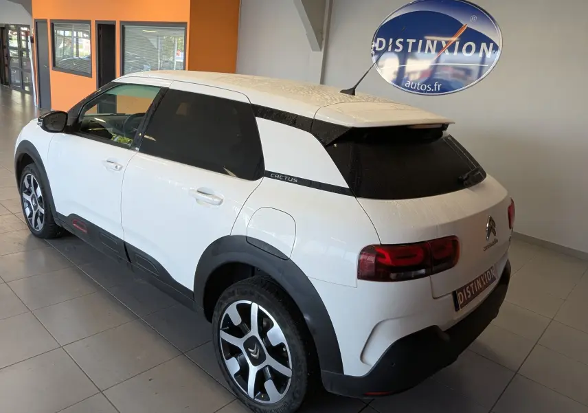 Vue 3/4 arrière droite d'une Citroën C4 Cactus blanche avec toit et détails noirs, roues alliage bicolores et vitres teintées.