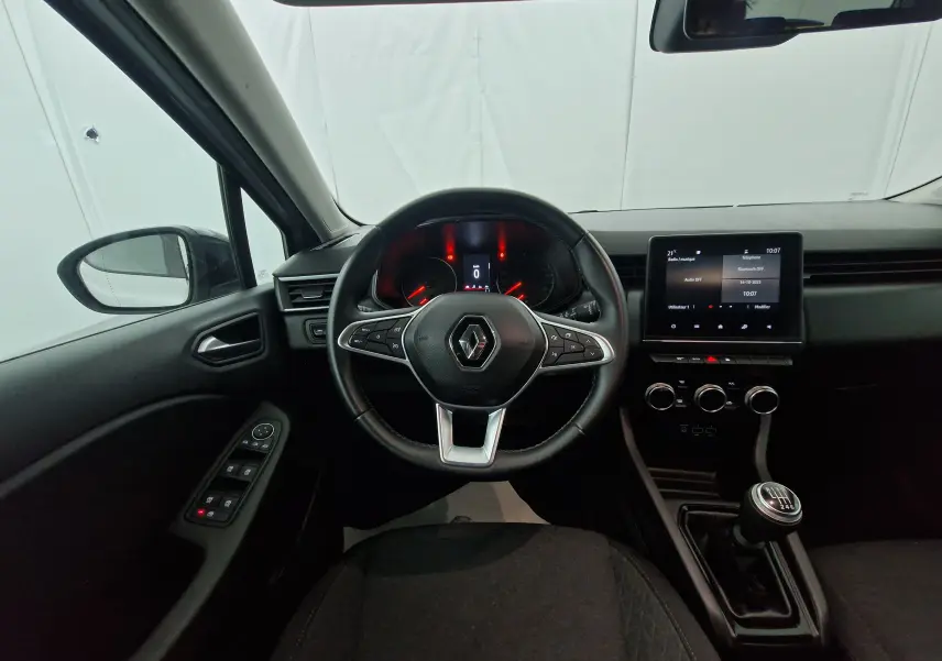 Vue intérieure centrée sur le volant et tableau de bord d'une Renault Clio V gris platine avec boîte manuelle et écran tactile.