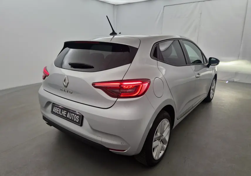 Renault Clio V gris platine vue 3/4 arrière droit dans un studio, feux arrière allumés et vitres teintées.