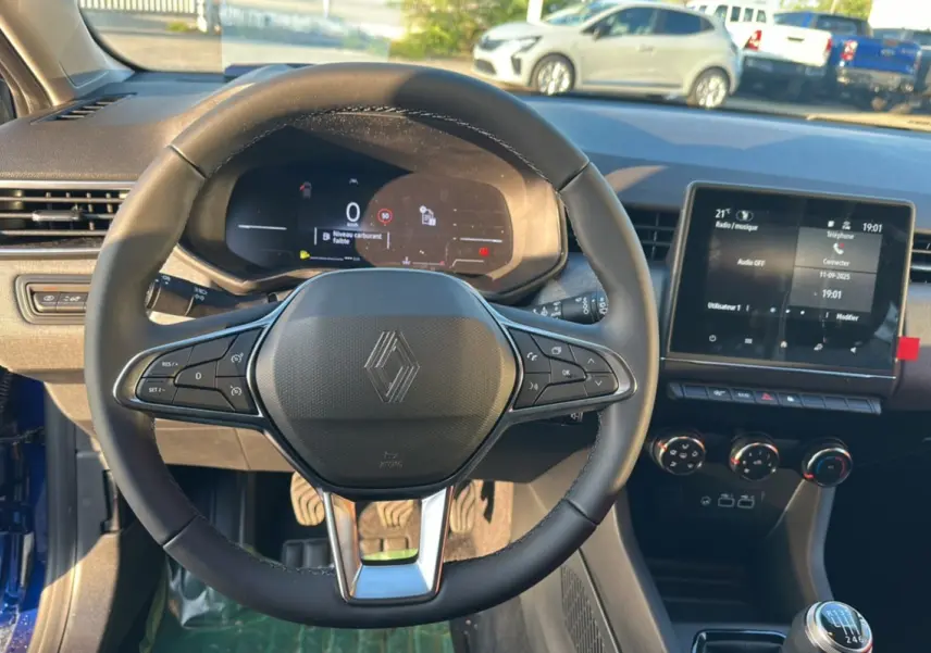 Vue intérieure centrée sur le volant Renault d'une Clio 2025 bleu iron, avec tableau de bord numérique et écran tactile.