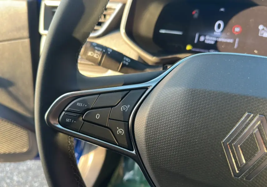 Gros plan sur le volant gauche de la Renault Clio DCI 100 Evolution Camera 2025 bleu iron, avec commandes de régulateur de vitesse.