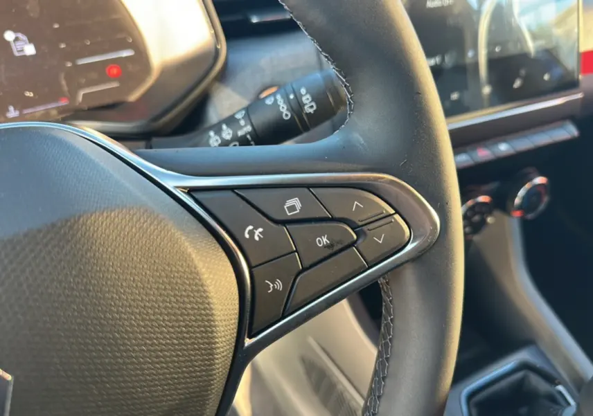 Gros plan sur les commandes du volant d’une Renault Clio 2025, finition DCI 100 Evolution Camera, intérieur noir.