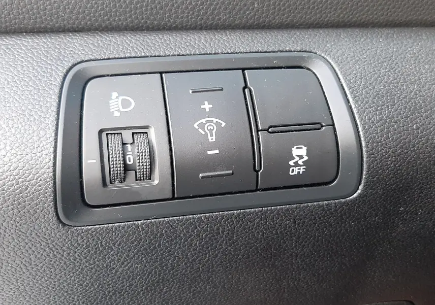 Gros plan sur les commandes noires de réglage des phares et de l'ESP dans l'habitacle d'une Hyundai i20 blanche de 2016.