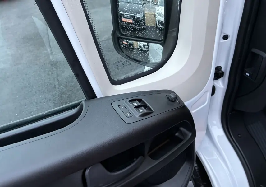 Vue intérieure côté gauche de la porte d’un Fiat Ducato Fourgon blanc 2025, avec commandes électriques des vitres et rétroviseur.