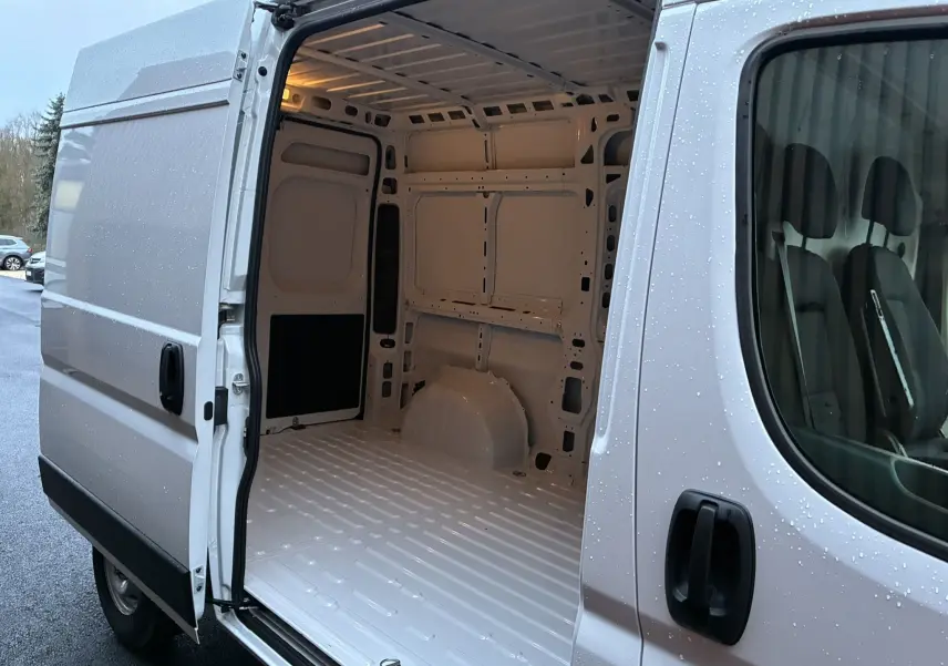 Vue latérale gauche du fourgon blanc Fiat Ducato 2.2 140 L2H2 2025 avec porte coulissante ouverte sur l’espace de chargement vide.