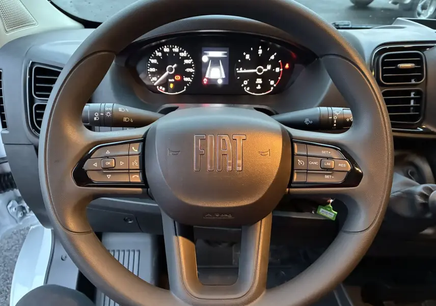 Vue rapprochée du volant noir du Fiat Ducato Fourgon 2025 avec commandes intégrées et tableau de bord numérique allumé.