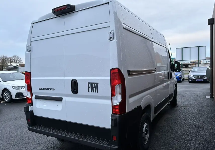 Vue 3/4 arrière droite d’un fourgon blanc Fiat Ducato 2.2 140 L2H2 avec portes arrière fermées sous ciel couvert.