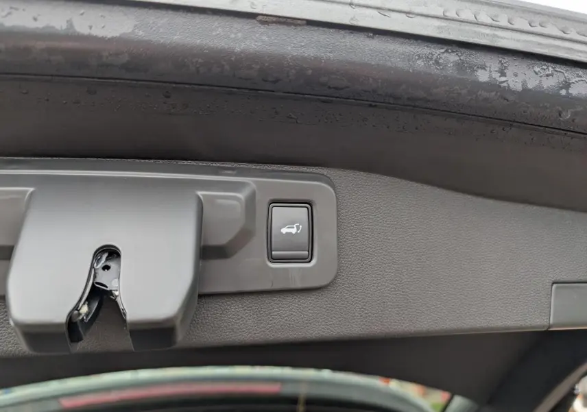 Gros plan sur le bouton d'ouverture motorisée du hayon intérieur d'un Renault Austral gris.