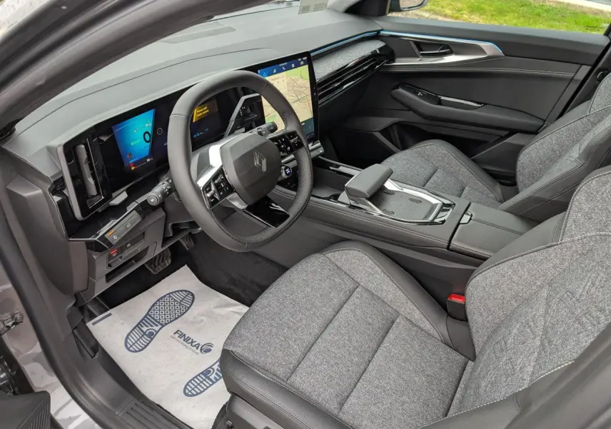 Vue intérieure côté conducteur du Renault Austral gris, mettant en valeur le tableau de bord numérique et les sièges tissu gris clair.