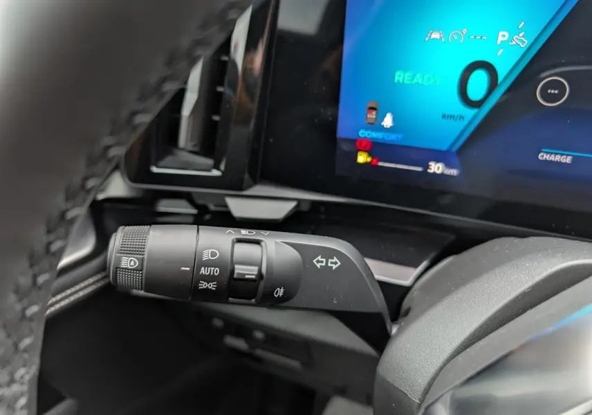 Gros plan sur la commande des feux et clignotants du tableau de bord du Renault Austral 2025, écran digital bleu en arrière-plan.