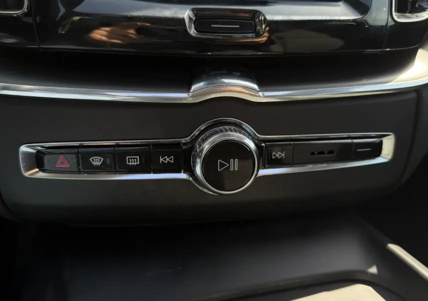 Gros plan sur la commande multimédia centrale chromée du tableau de bord du Volvo XC60 blanc Crystal 2024.