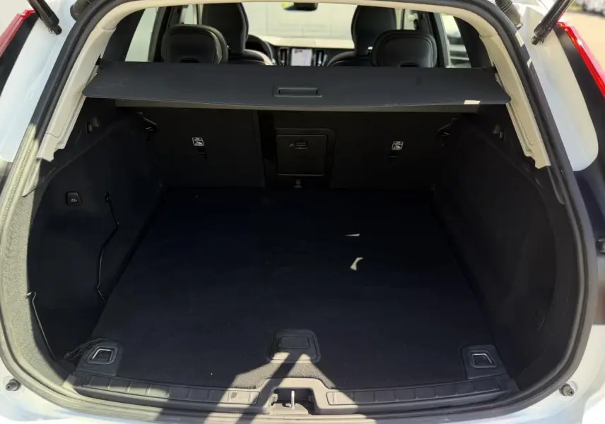 Coffre ouvert vu de l'arrière d'un Volvo XC60 blanc Crystal 2024 avec cache-bagages noir.