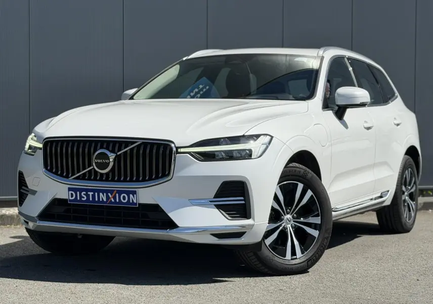 Volvo XC60 T6 AWD PHEV blanc Crystal en 3/4 avant droit, avec calandre chromée et jantes alliage 18 pouces.