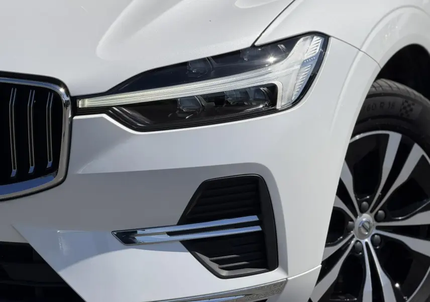 Gros plan sur l'avant droit du Volvo XC60 blanc Crystal, mettant en valeur le phare LED et la jante alliage noire et argent.