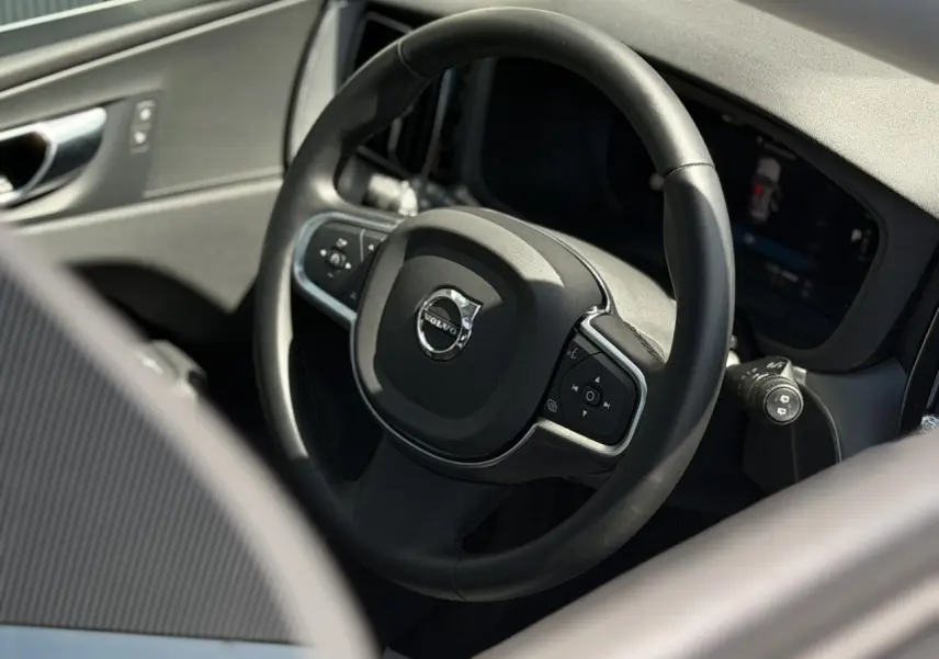 Gros plan sur le volant noir simili-cuir du Volvo XC60 2024, avec commandes intégrées et tableau de bord digital.