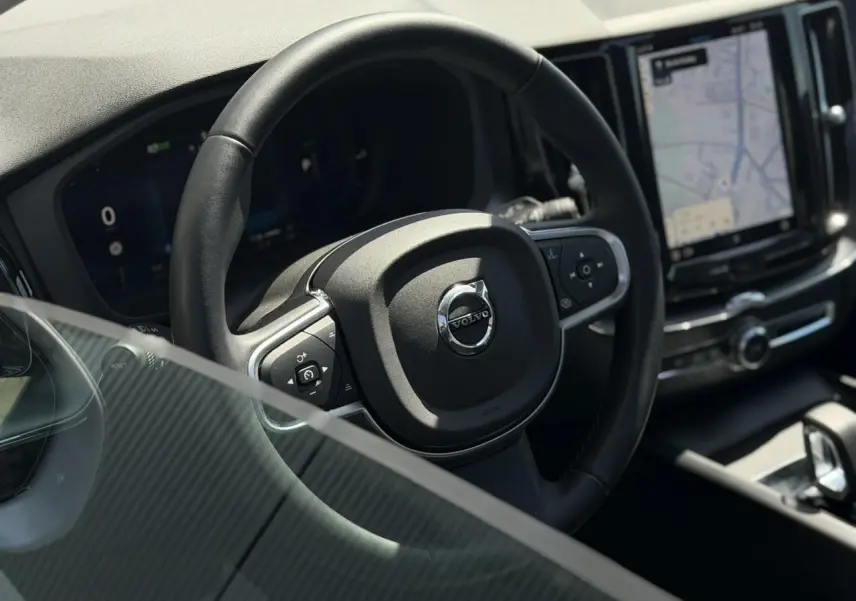 Vue rapprochée du volant noir en simili-cuir du Volvo XC60 2024 avec écran tactile et tableau de bord digital.