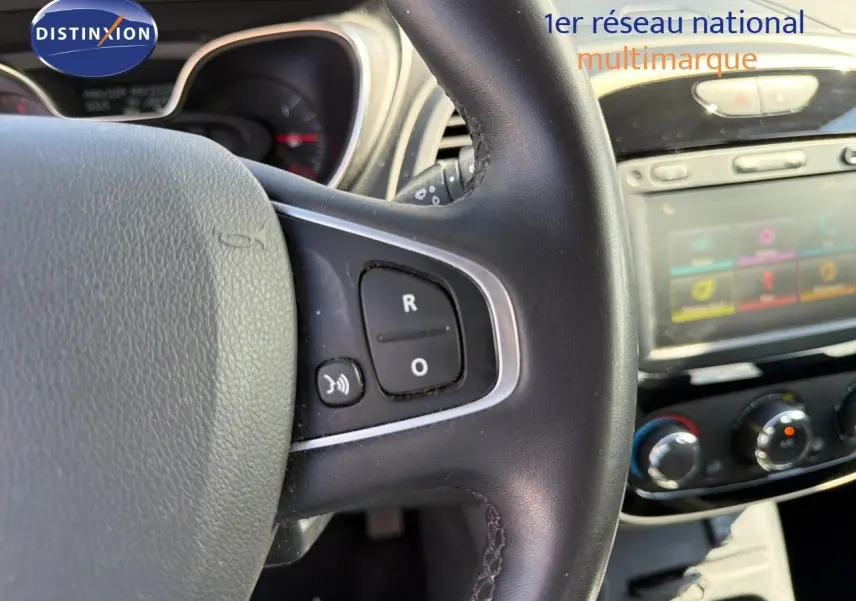 Gros plan sur le volant noir du Renault Captur gris Cassiopée, avec commandes audio visibles et tableau de bord en arrière-plan flou.