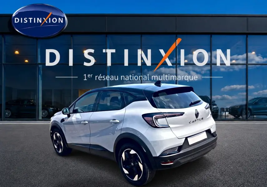 Vue 3/4 arrière droite d'un Renault Captur 1.2 TCe 115 Techno blanc Rafale avec toit noir devant un showroom Distinxion.