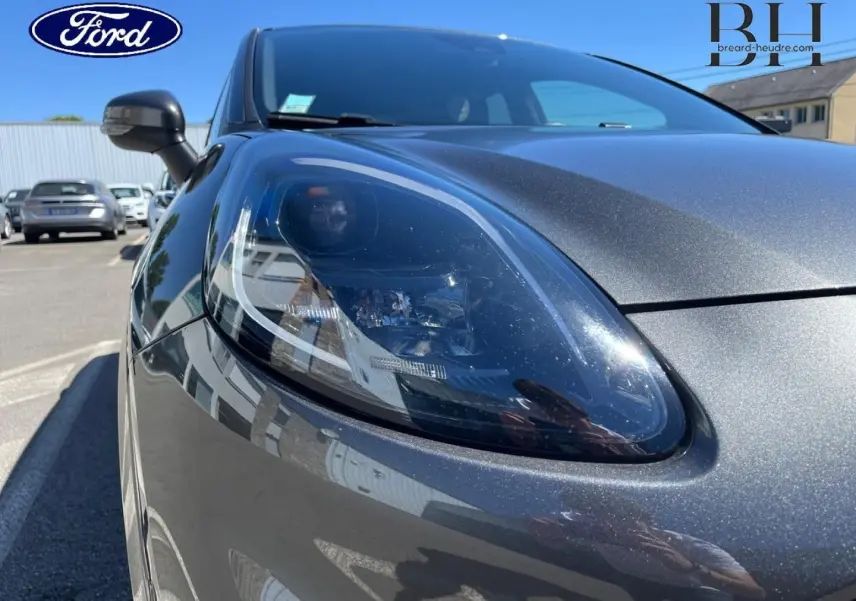 Gros plan sur le phare avant gauche du Ford Puma 2024 gris Solar métallisé sous un ciel dégagé.