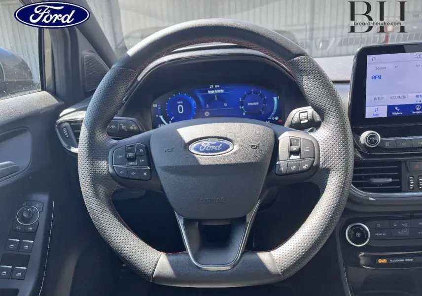 Vue intérieure centrée sur le volant perforé avec surpiqûres rouges du Ford Puma 2024, tableau de bord digital et écran tactile.