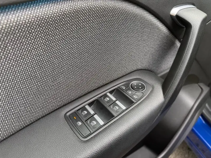 Gros plan sur la commande des vitres électriques côté conducteur du Renault Captur 2025, avec intérieur noir et bleu visible.