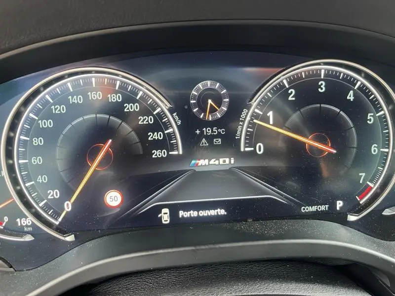 Vue rapprochée du tableau de bord digital du BMW X3 M40iA 2019 affichant la vitesse, le régime moteur et l'alerte porte ouverte.