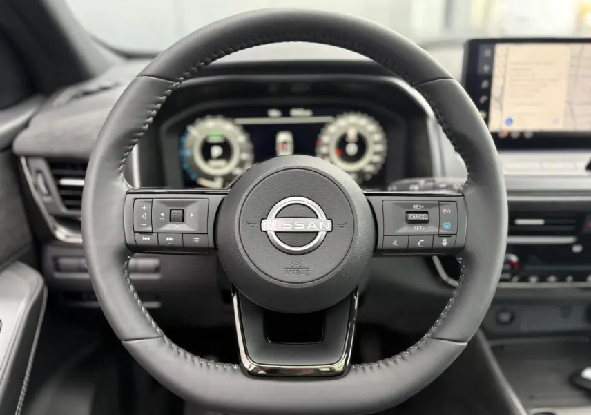 Volant cuir noir du Nissan Qashqai 2025 avec commandes intégrées et tableau de bord numérique en arrière-plan.