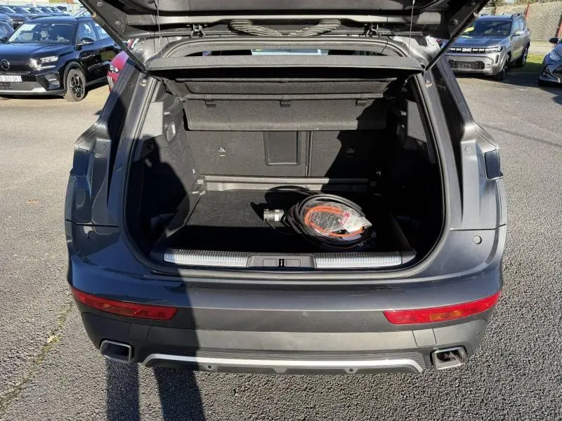 Vue arrière ouverte du coffre du DS7 E-TENSE gris titane 2024, montrant le câble de recharge hybride dans un parking.