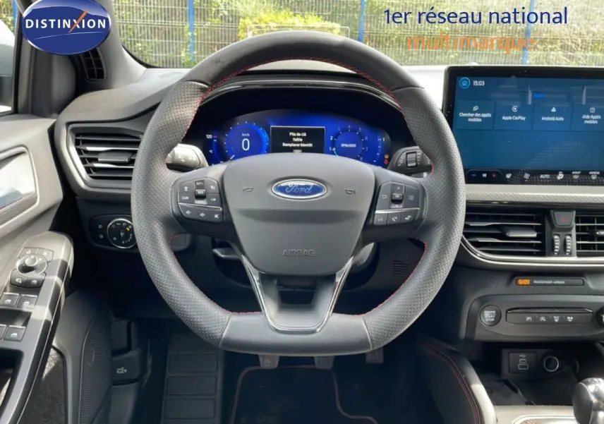 Vue intérieure centrée sur le volant perforé avec coutures rouges et tableau de bord numérique de la Ford Focus SW 2023.