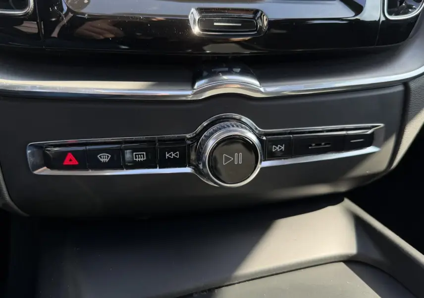Gros plan sur la commande centrale multimédia noire avec boutons de lecture et alertes du Volvo XC60 gris Dusk 2024.