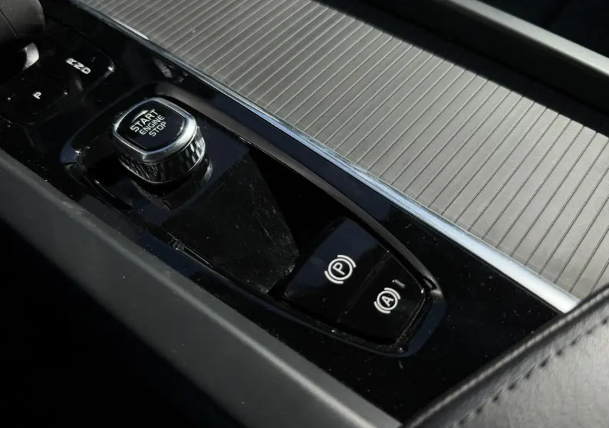 Gros plan sur la console centrale noire du Volvo XC60 T6 AWD PHEV 2024 avec bouton Start/Stop et frein à main électronique.