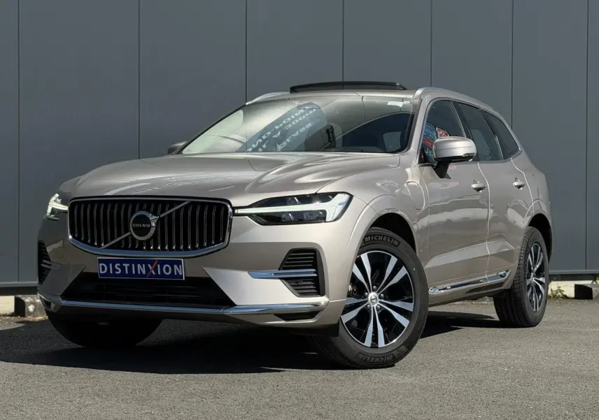 Volvo XC60 T6 AWD PHEV gris Dusk en 3/4 avant droit, avec jantes alliage et contours chromés visibles.