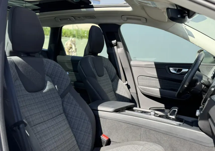 Intérieur avant du Volvo XC60 T6 AWD PHEV 2024, sièges en tissu gris à motif, toit ouvrant panoramique visible.