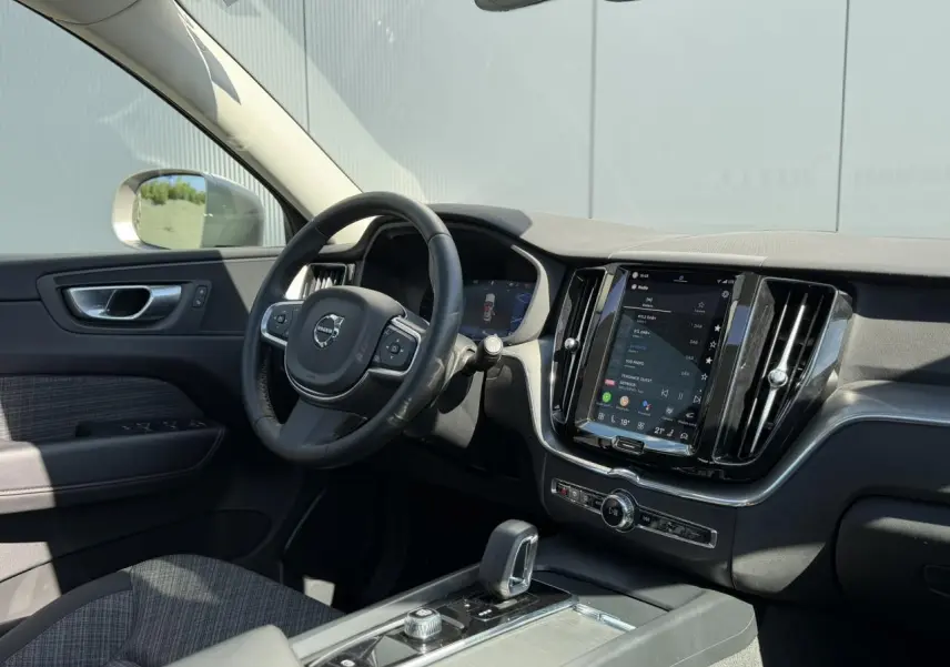 Vue intérieure côté conducteur du Volvo XC60 2024, avec tableau de bord noir et écran tactile vertical.