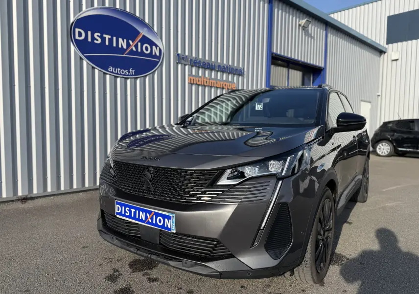 Peugeot 3008 gris en 3/4 avant droit, avec calandre noire et phares LED distinctifs, stationné devant un bâtiment.