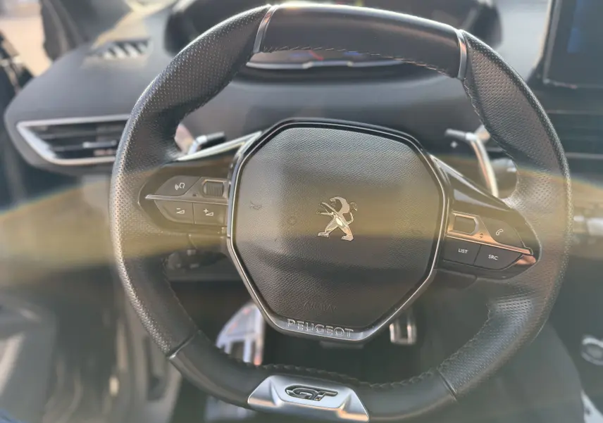Vue rapprochée du volant cuir noir du Peugeot 3008 2022 avec logo lion et badge GT en bas.