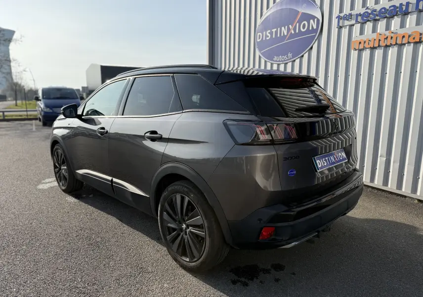 Vue 3/4 arrière droite d’un Peugeot 3008 gris 2022 avec hayon électrique et jantes noires, stationné devant un mur métallique.