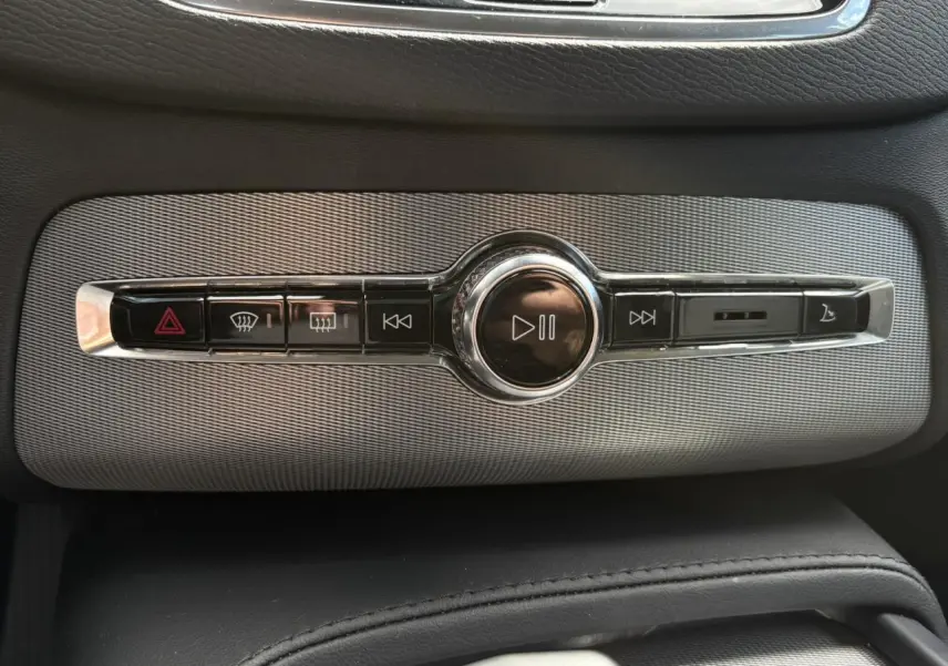Gros plan sur la commande centrale multimédia chromée du Volvo XC90 T8 gris Dusk, avec boutons de lecture et alertes.